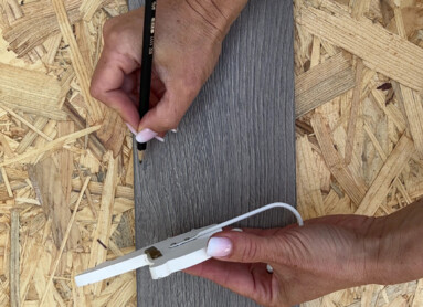 Eine Person markiert mit einem Bleistift Positionen auf einem Stück Laminat mit Tiermotiven.