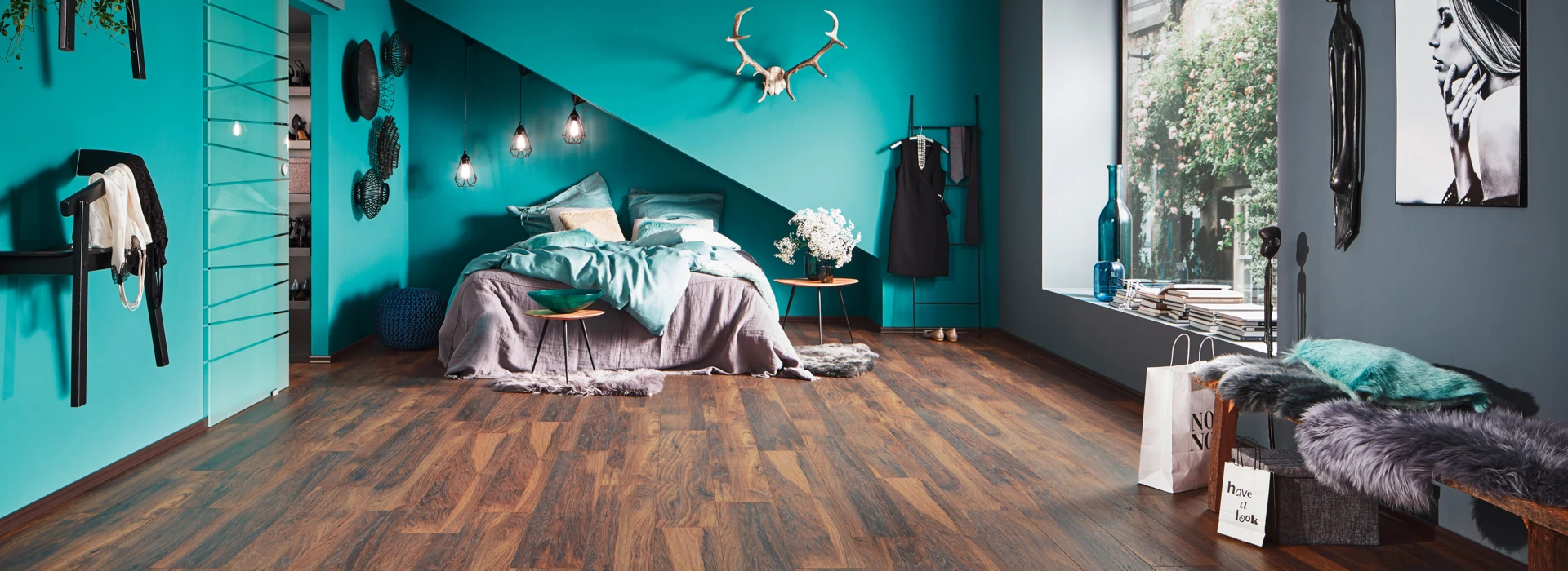 Bedroom with teal walls, stylish decor, and dark laminate flooring, featuring a cosy bed and large window with natural light.