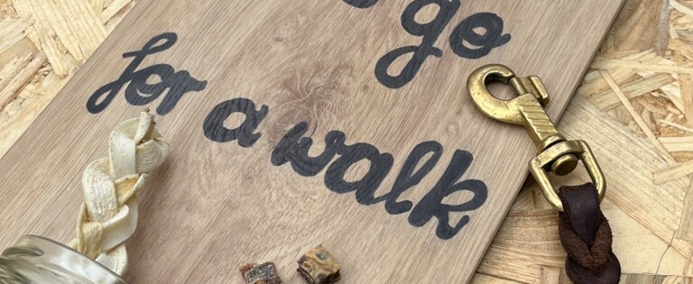 Eine Tafel mit der Aufschrift "Let's go for a walk", Hundekotbeutel, Leine und Leckerlis auf Laminatboden.