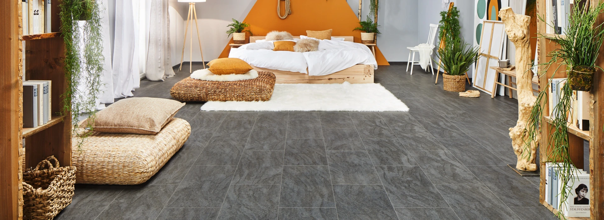 Gemütliches Schlafzimmer mit grauem Laminatboden der Serie 'Ceramico', orangefarbener Wand und natürlichen Dekorationen.