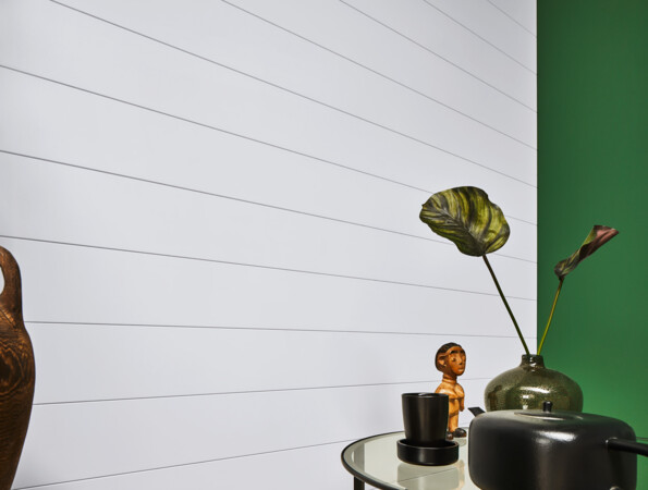 Ein stilvoll dekorierter Raum mit weißen Wandpaneelen der Serie 'Variation', grüner Wand, Keramikvase und Pflanzen auf einem Tisch.