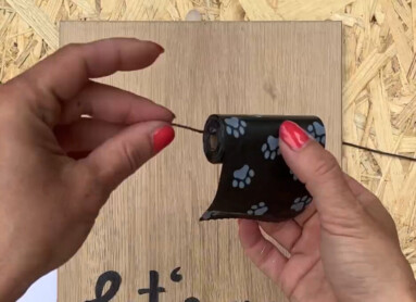 Hände halten Hundekotbeutel über einem Holzbrett mit "Let's go for a walk"-Text, daneben ein Lineal und ein leeres Glas.