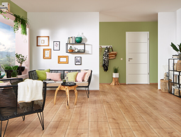 Wohnraum mit hellen Laminatböden, schwarzem Mobiliar und grüner Wand, dekoriert mit Pflanzen und Bildern.