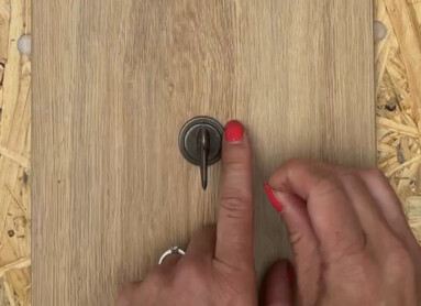 Eine Holzplatte mit der Aufschrift "Let's go for a walk" und einer Hand, die einen Haken berührt. Laminatboden und Farn im Hintergrund.