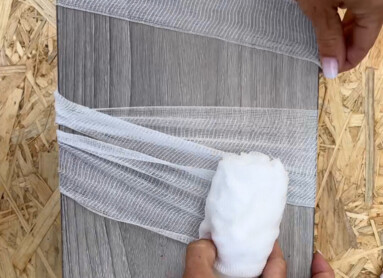 Eine Person wickelt weißes Netzgewebe um ein graues Holzbrett.