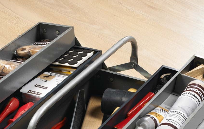 Werkzeugkasten mit Zubehör zur Verlegung von Laminatboden auf hellem Boden.