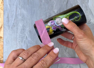 Eine Person wickelt ein rosa Band um eine bedruckte Dose auf einer Holzoberfläche.