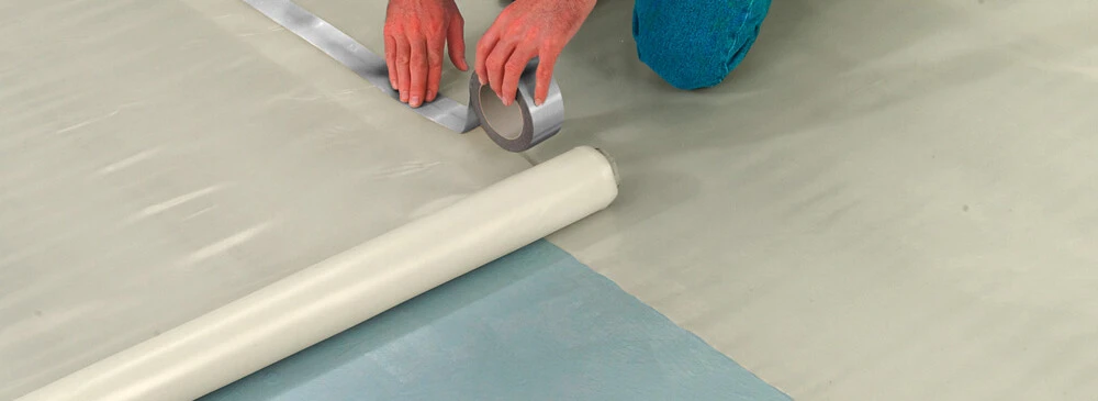 Ein Mann klebt eine Unterlage für Laminatboden auf den Boden.
