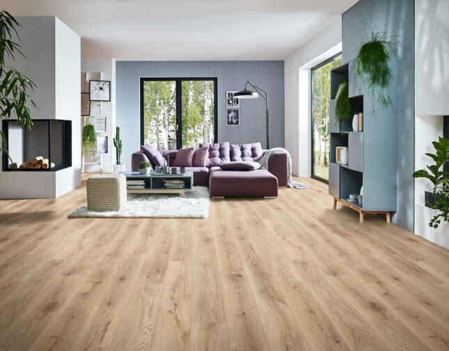 Living room with light laminate flooring, a purple sofa, large windows, and green plants.