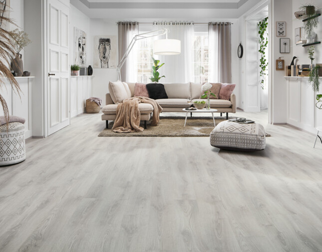 Wohnzimmer mit hellem Laminatboden, beigem Sofa, Pflanzen und dekorativem Teppich.