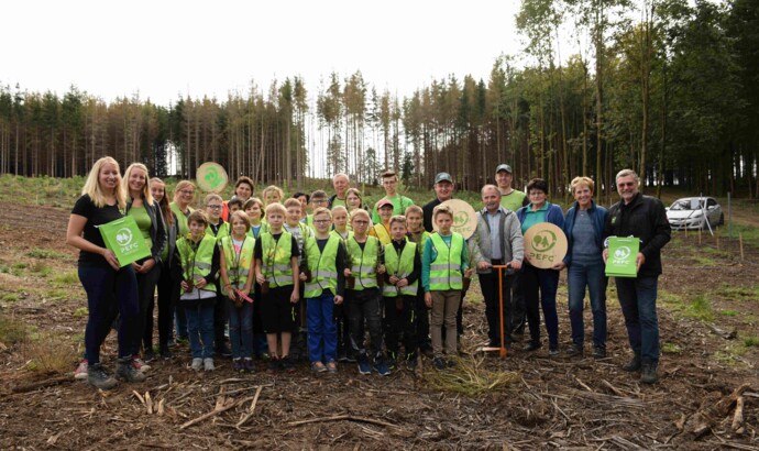 Eine Gruppe von Erwachsenen und Kindern in Sicherheitswesten steht in einem Wald mit PEFC-Zertifizierungslogos.