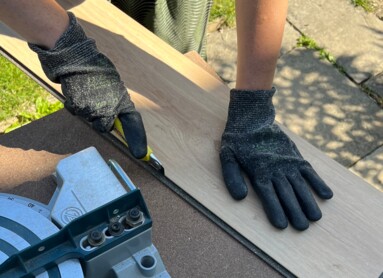 Eine Person schneidet Laminatboden mit einer Kreissäge im Freien.
