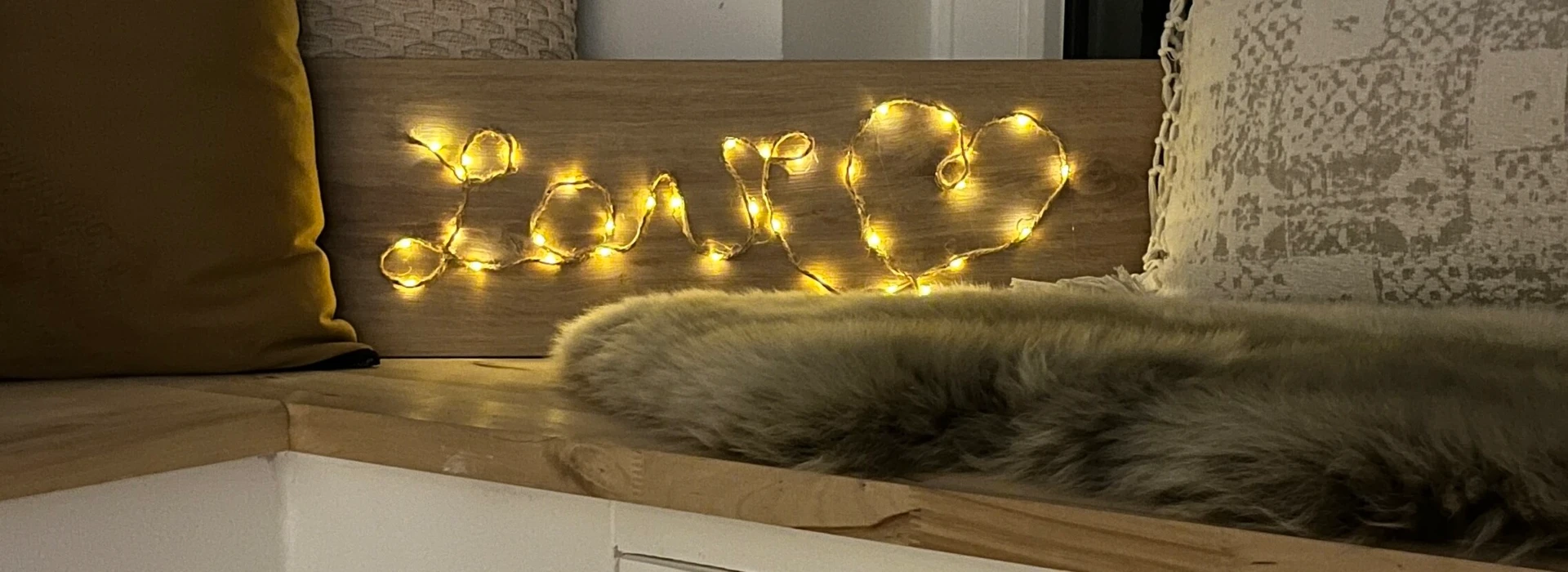 Gemütliche Ecke mit Sitzkissen und Lichterkette, die "Love" auf einem Holzbrett formen.