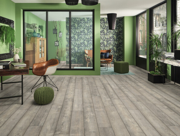 Modernes Wohnzimmer mit grünem Dekor, großen Fenstern und hellem Laminatboden. Pflanzen und stilvolle Möbel ergänzen das Ambiente.