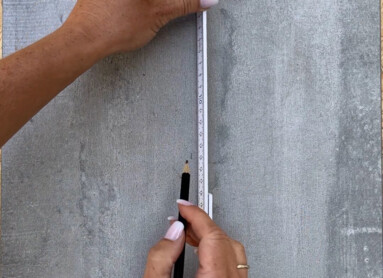 Eine Person misst eine graue Fliese auf einer Holzoberfläche mit einem Maßband für Laminatbodeninstallation.