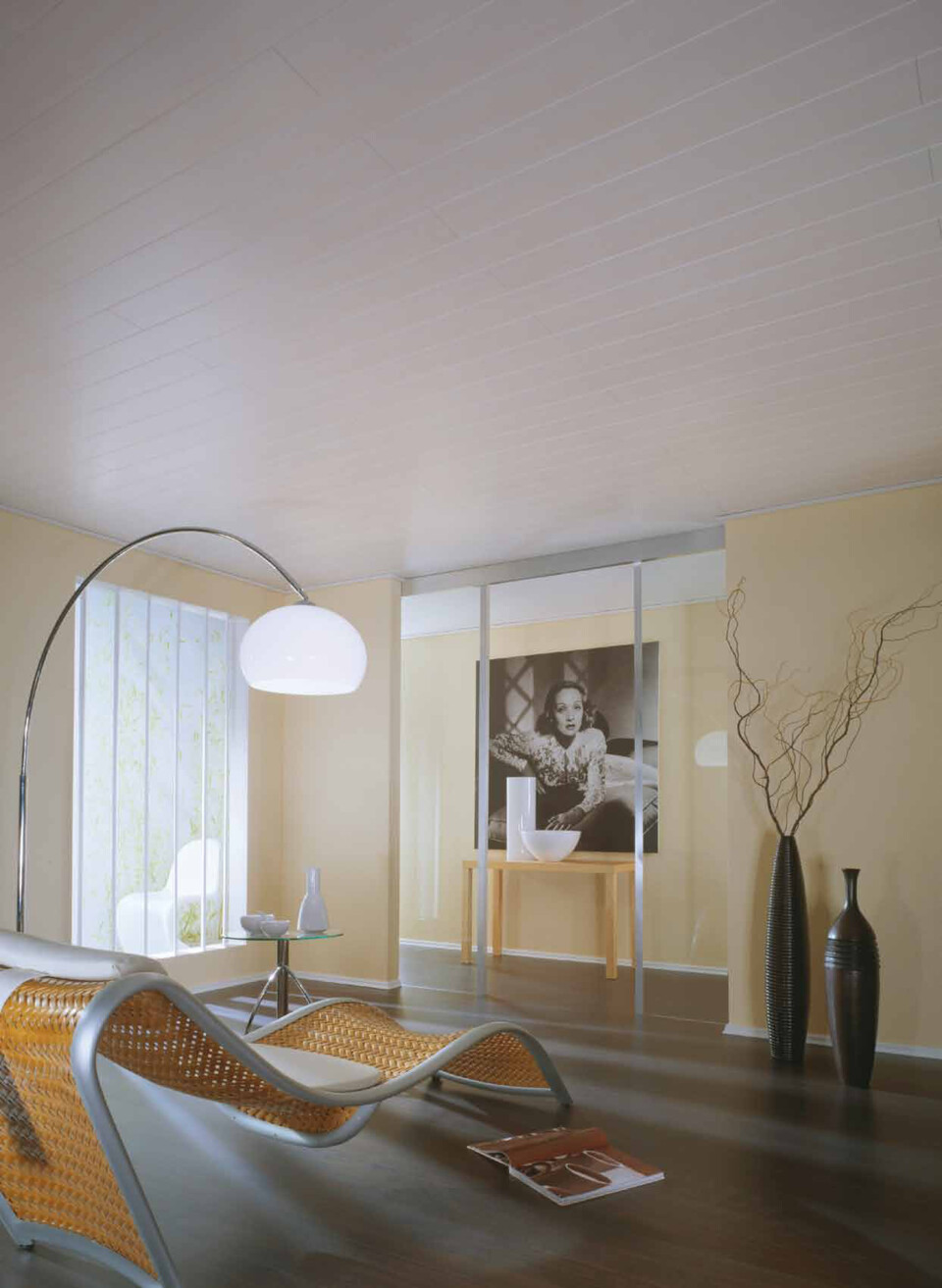 Modernes Wohnzimmer mit geschwungenem Rattan-Liege, großem Lampenbogen, Vasen und Kunstwerk an der Wand.