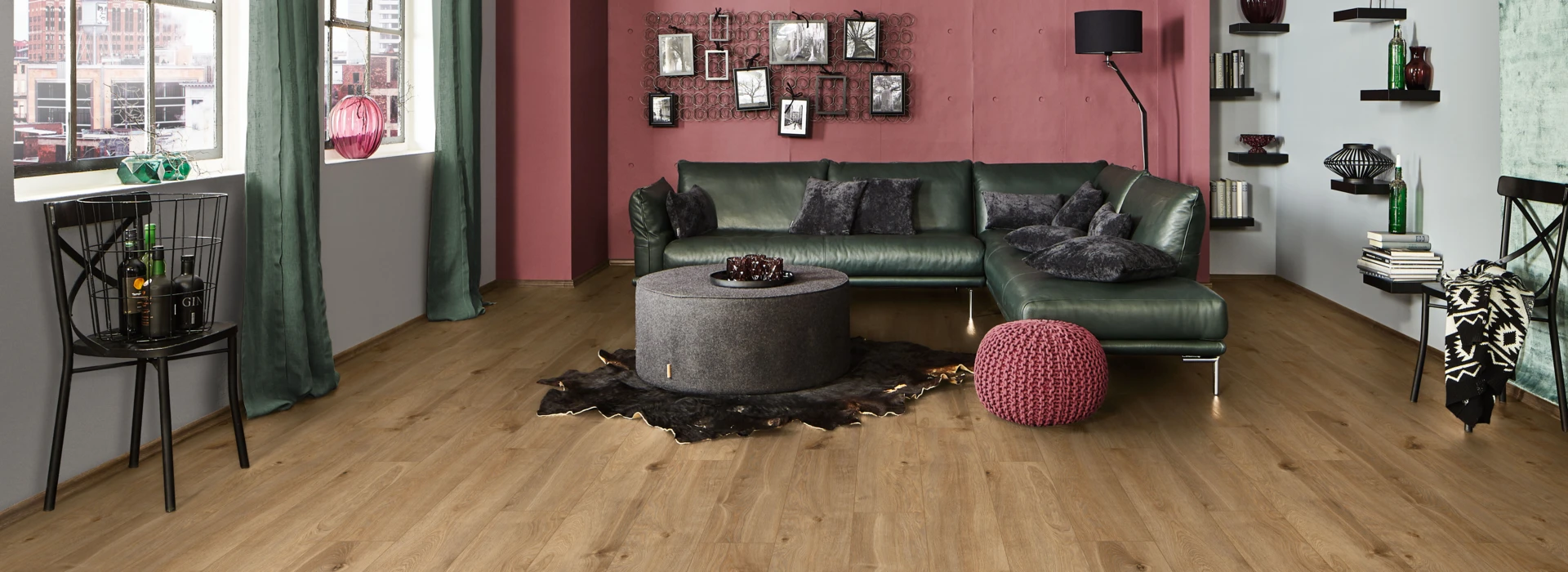 Spacious living room with laminate flooring from the series 'Vinto', green leather sofa, and red accents.