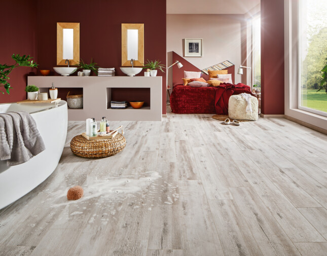 Luxurious bathroom with white laminate flooring, featuring a bathtub, double sinks, and a view of a cozy bedroom with red accents.