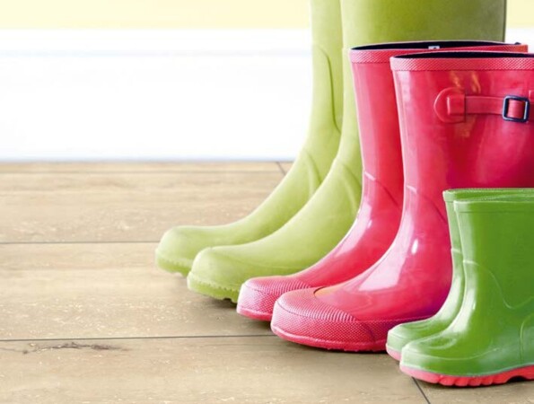 Bunte Gummistiefel auf einem Laminatboden vor einer gelben Wand.