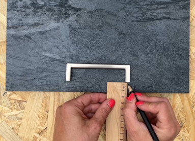 Hand zeichnet mit Lineal und Stift auf einer dunklen Oberfläche, vorbereitet für Laminatbodenprojekt.
