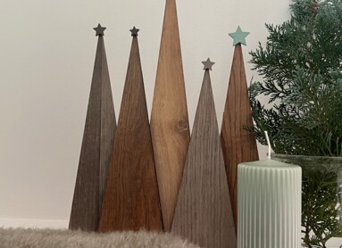 Dekoration mit Holz-Weihnachtsbäumen, grünem Zweig und Kerze auf Teppich.