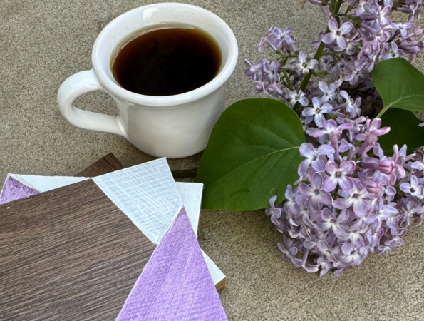 Kaffeetasse neben Fliederblüten und dekorativen Laminatbodenmustern auf Beton.
