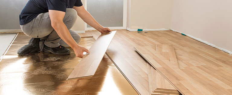 Ein Mann verlegt Laminatboden in einem Raum mit hellem Holzdesign.