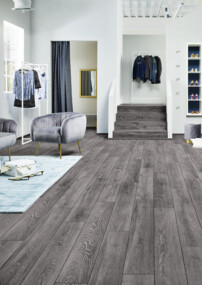 Innenausstattung eines Bekleidungsgeschäftes mit grauem Laminatboden, stilvollen Sesseln und Regalen voller Schuhe und Kleidung.