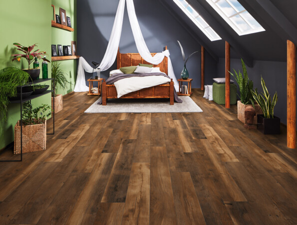 Ein Schlafzimmer mit Dachschräge und dunklem Laminatboden der Serie 'Vinto'. Das Zimmer hat eine grüne Wand mit Pflanzen und unter den Dachfenstern steht ein Himmelbett.