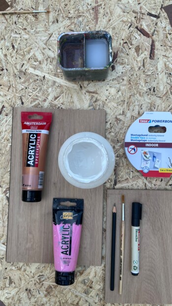 Acrylfarben, Pinsel, Bleistifte und doppelseitiges Klebeband auf Laminatboden.