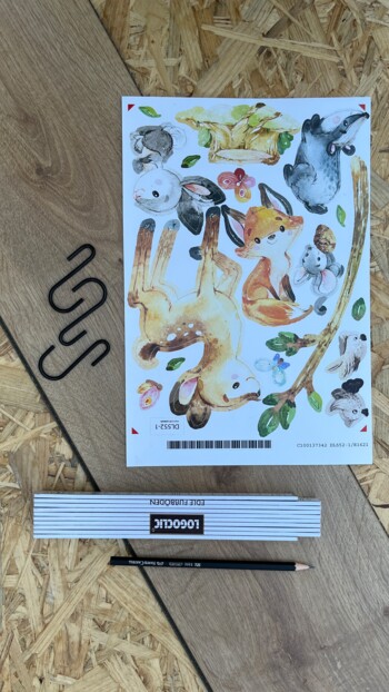 Tieraufkleber, Zollstock und Bleistift auf Laminatbodendiele.