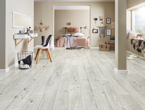 Moderner Raum mit hellem Laminatboden, gemütlicher Einrichtung und Dekoration. Schlafzimmer im Hintergrund mit Bett und Wanddekorationen.