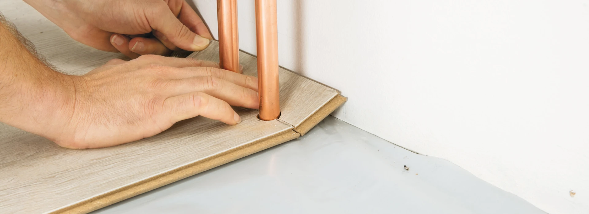Hände installieren Laminatboden um Heizungsrohre.