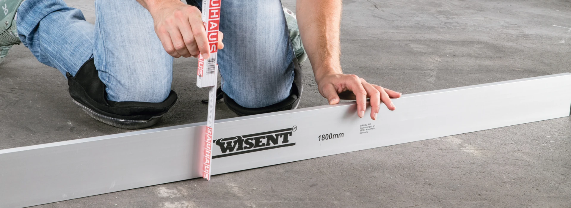 Ein Mann misst mit einem Maßband auf einem Betonboden, neben einem 1800mm langen Aluminiumprofil.