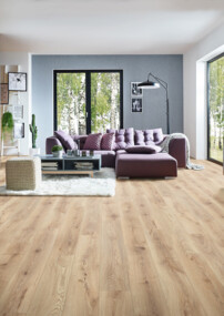 Wohnzimmer mit hellem Laminatboden, violetter Couch, Kamin und Pflanzen, beleuchtet von großen Fenstern.