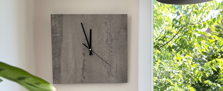 Gemütliche Ecke mit Kissen, Wanduhr und Pflanzen, neben einem Fenster mit Blick ins Grüne.