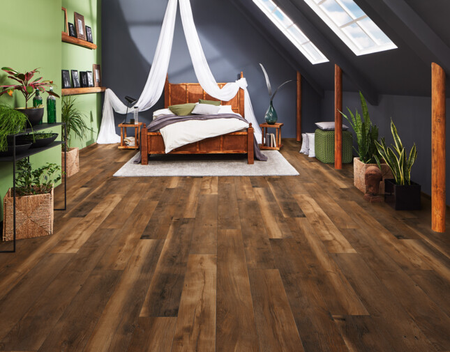 Ein Schlafzimmer mit Dachschräge und dunklem Laminatboden der Serie 'Vinto'. Das Zimmer hat eine grüne Wand mit Pflanzen und unter den Dachfenstern steht ein Himmelbett.
