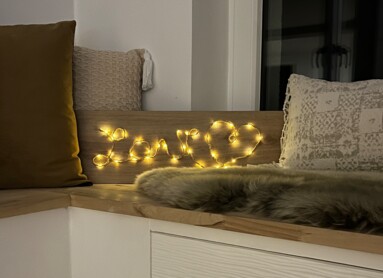 Gemütliche Ecke mit Sitzkissen und Lichterkette, die "Love" auf einem Holzbrett formen.