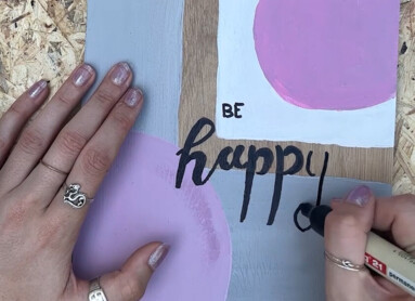 Person bemalt Laminatboden mit Blumen und "Be happy" Schriftzug.