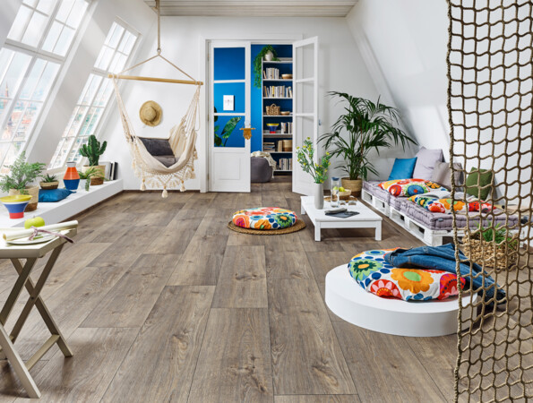 Bright room with laminate flooring, featuring a hammock, colourful cushions, plants, and a bookshelf, creating a cosy and inviting atmosphere.
