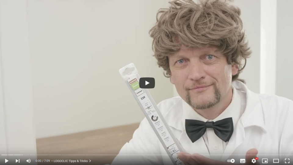 Ein Mann in weißem Kittel und Fliege hält ein LOGOCLIC<sup>®</sup>-Produkt in die Kamera.