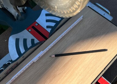 Kreissäge schneidet Laminatboden mit Maßband und Bleistift auf Werkbank.