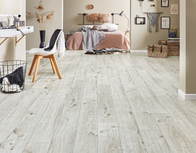 Bedroom with light laminate flooring, beige walls, and stylish decor, including a bed, chair, and desk.