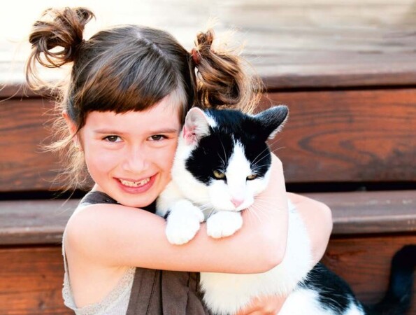 A young girl hugging a black and white cat on wooden steps.