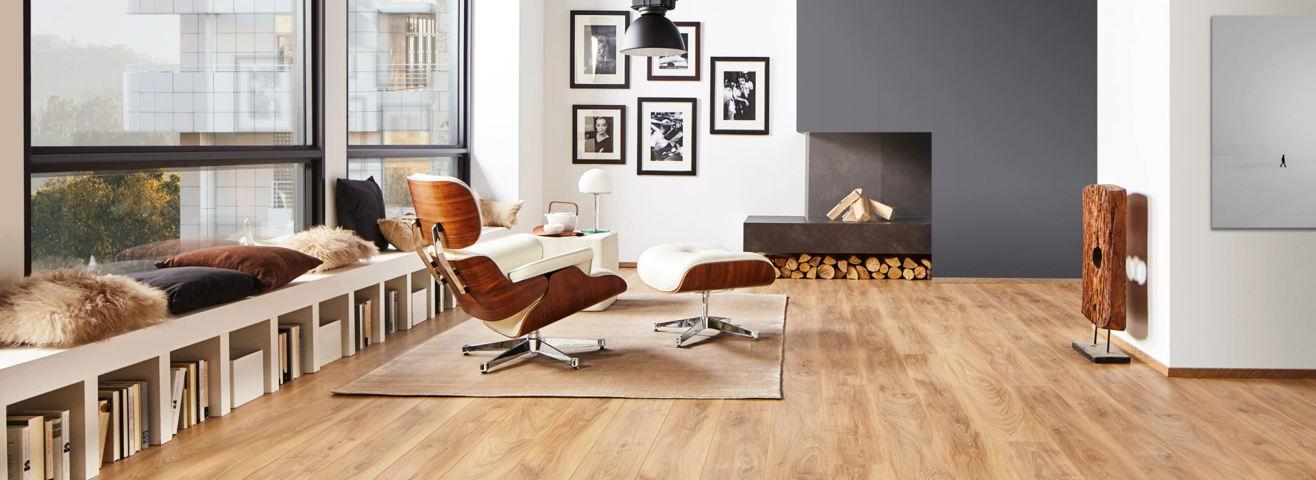 Spacious living room with light laminate flooring, featuring a cosy seating area, fireplace, and large windows.