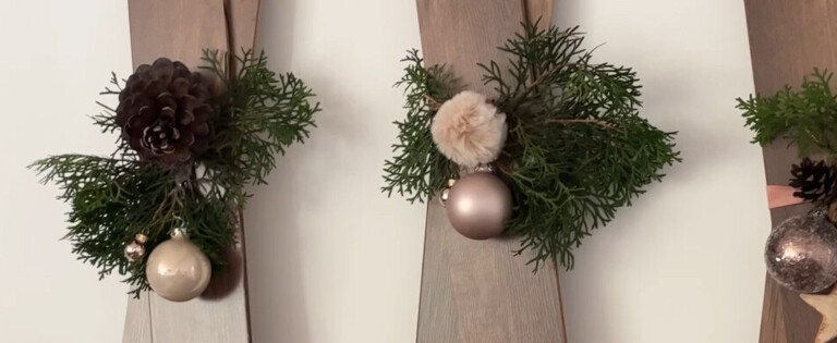 Dekorative Holzlatten mit Weihnachtsschmuck und Tannenzweigen an einer Wand, darunter ein flauschiger Teppich.