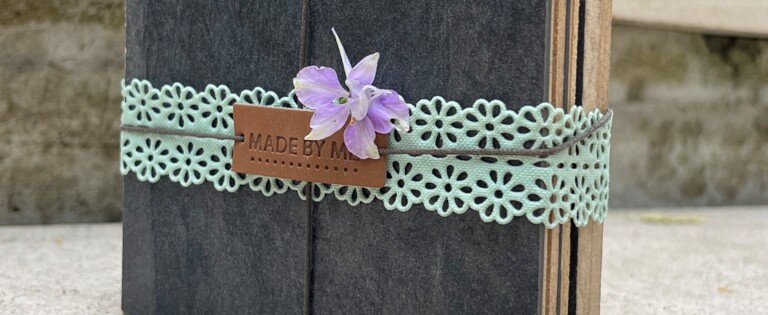 Kleines Buch mit grünem Spitzenband und Blume, im Freien auf Steinoberfläche platziert.