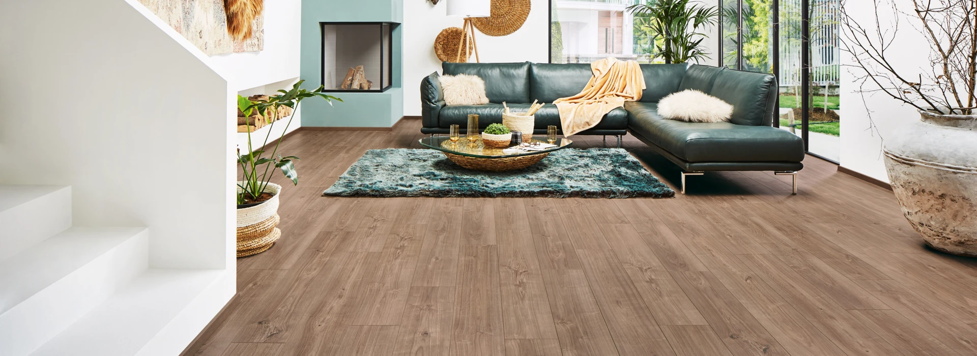 Spacious living room with stylish laminate flooring, teal sofa, and large windows overlooking greenery.