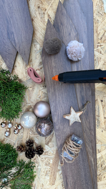 DIY-Projekt mit Laminatboden, Heißklebepistole, Weihnachtskugeln, Sterne und Tannenzweigen zur festlichen Dekoration.