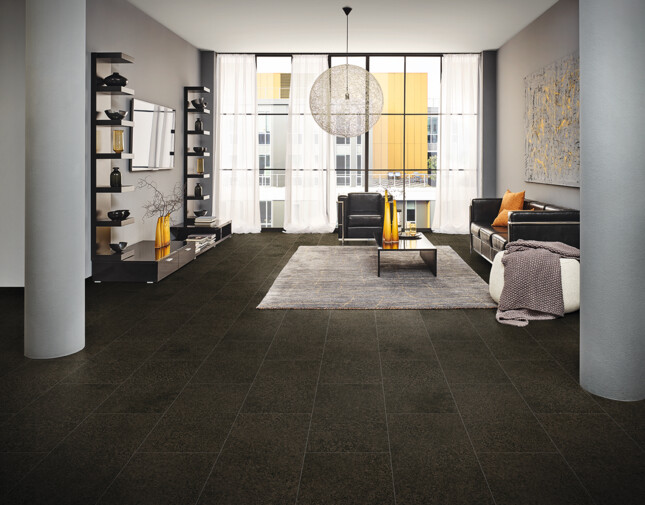 A stylish living room with dark laminate flooring, featuring a large window, black sofas, and decorative shelves.
